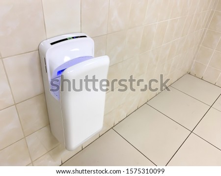 White modern hand dryer with blue lighting hanging on the wall in a public toilet, WC