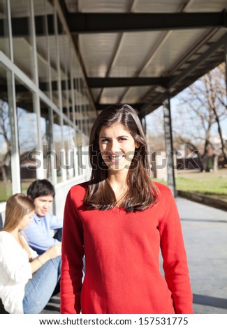 Portrait of happy young woman smiling with students in background on college campus