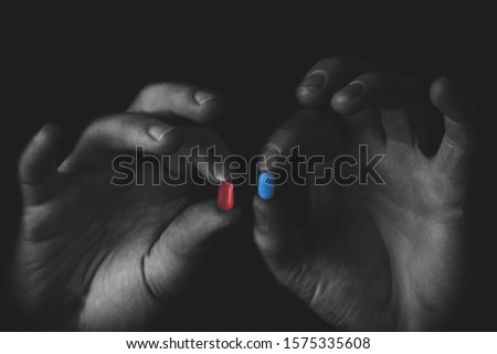 Man holding red and blue pills in hand isolated on black background.  Medicine concept and pills, copy space Royalty-Free Stock Photo #1575335608
