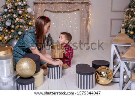 Mother gives Christmas gift to his little son for a New Year. Mom and son opening Christmas presents.