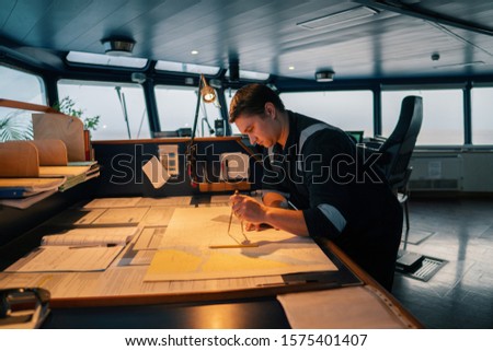 Marine navigational officer during navigational watch on Bridge . He does chart correction of nautical maps and publications. Work at sea Royalty-Free Stock Photo #1575401407