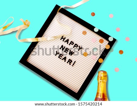                          Top view of a letter board with " happy new year" message on a bright teal background, with a bottle of champagne and confetti       