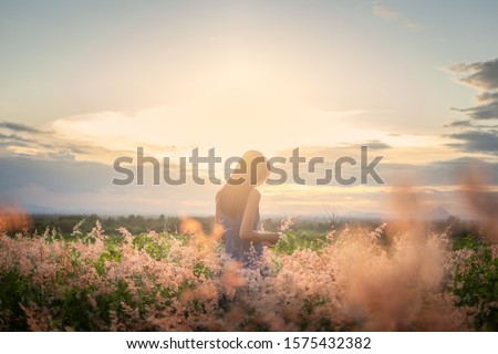 Trendy girl in stylish summer dress feeling free in the field with flowers in sunshine.