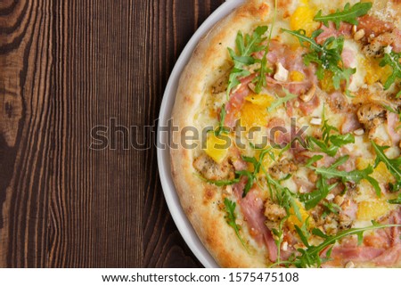 Pizza with turkey, bacon, orange and cashew nuts on dark wooden background