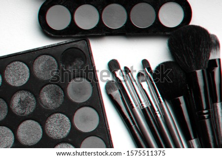 set of professional makeup brushes and a palette with multi-colored eye shadows on a pink background. Black and white photo with 3D glitch effect