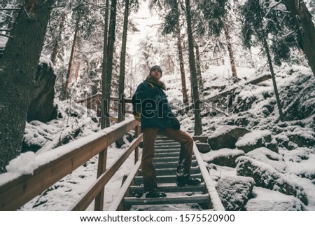 Picture of man in winter forest on wooden bridge .