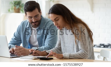 Young husband and wife using calculator laptop computer manage finances calculate bills tax talk doing paperwork together sit at home table discuss family mortgage loan money payment planning budget Royalty-Free Stock Photo #1575538927