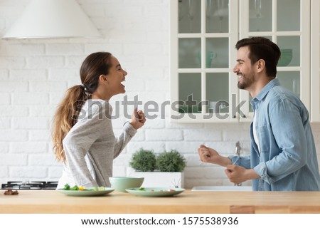 Happy active young family couple dancing having fun together preparing healthy food at home, carefree husband and wife laughing cooking dinner meal listening music enjoy dance in modern kitchen