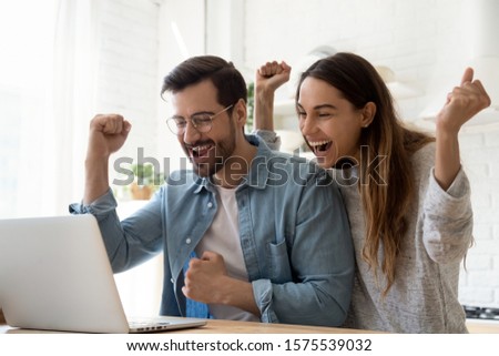 Excited overjoyed young family couple winners feel lucky got sale discount offer by email look at laptop screen celebrate online victory internet auction bid lottery win in app computer technology Royalty-Free Stock Photo #1575539032