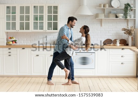 Happy romantic young couple bonding dancing in modern kitchen with white furniture enjoy sweet moments of affection, cheerful husband and wife celebrating anniversary having fun at home lifestyle Royalty-Free Stock Photo #1575539083