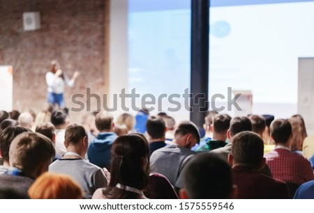 Adult people at conference listen to woman speaker providing lecture on scene in big conference hall. Business and Entrepreneurship concept. Audience at the conference hall. Royalty-Free Stock Photo #1575559546