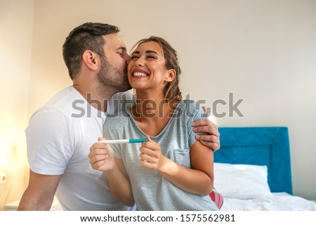 Young couple is happy because of positive pregnancy test. Affectionate couple finding out results of a pregnancy test in their bedroom. Family, parenting and medical concept