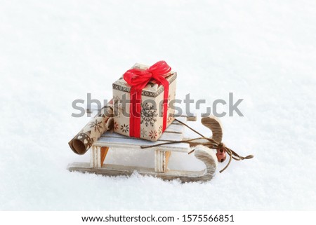 Toy wooden sled with a Christmas gift and a scroll with wishes on the background of snow. Close up, daylight. White background. Free space. Christmas card.