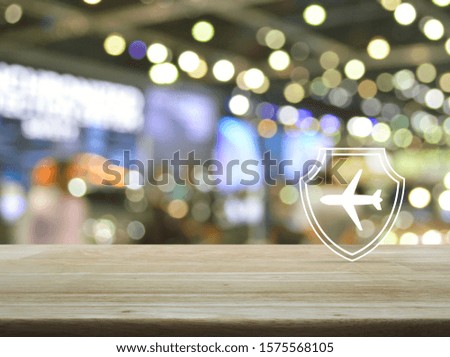 Airplane with shield flat icon on wooden table over blur light and shadow of shopping mall, Business travel insurance and safety concept