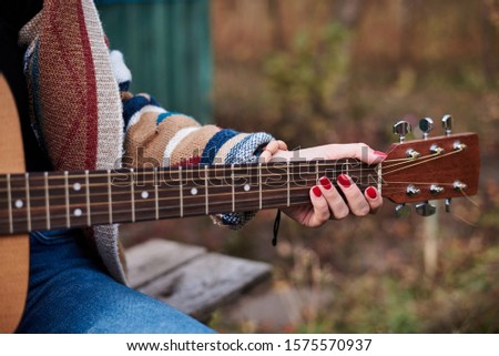 Young woman, wearing colorful cardigan, playing acoustic guitar, Close-up picture of guitar fingerboard, held in hands with bracelets of hippie musician. Playing guitar.