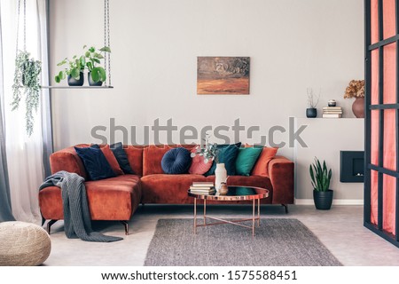 Real photo of colorful pillows on a red corner couch in white living room interior with gray rug