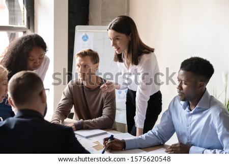 Young female employee sharing point of view with focused diverse teammates at brainstorming meeting. Group of international employees discussing project ideas, financial report, marketing strategy. Royalty-Free Stock Photo #1575620548