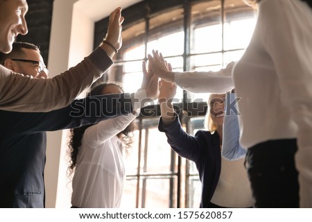 Overjoyed older and younger teammates joining hands in air, giving high five, celebrating shared company success in business meeting. Happy diverse colleagues coming to common decision, showing unity. Royalty-Free Stock Photo #1575620857