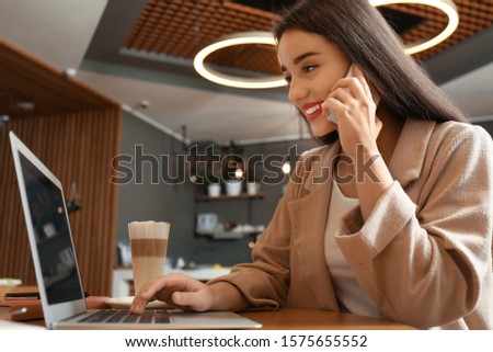 Young blogger with laptop talking on phone in cafe