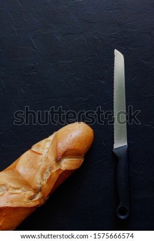 BREAD BAR NEXT TO KITCHEN KNIFE ON DARK BACKGROUND WITH TEXTURE