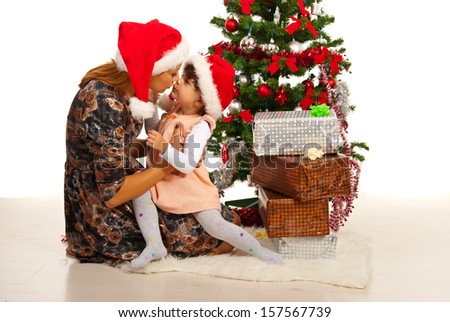 Mother kissing her daughter near Xmas tree with presents
