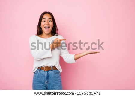 Young mixed race indian woman excited holding a copy space on palm.