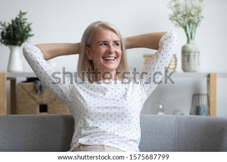Satisfied middle-aged 60s woman sitting on couch put hands behind head smiling enjoy carefree time at home, no stress and anxiety, reducing fatigue and tiredness, relish of retired calm life concept Royalty-Free Stock Photo #1575687799