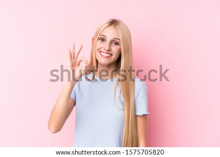 Young blonde woman on pink background cheerful and confident showing ok gesture.