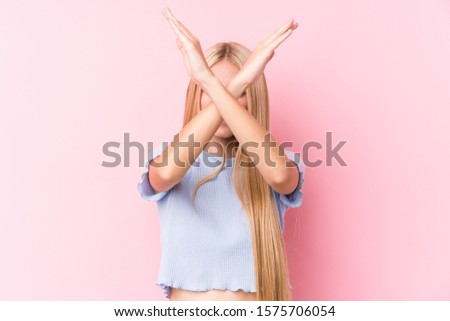 Young blonde woman on pink background keeping two arms crossed, denial concept.