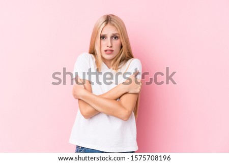 Young blonde woman on pink background going cold due to low temperature or a sickness.