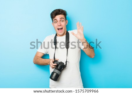Young caucasian photographer man holding a camera celebrating a victory or success