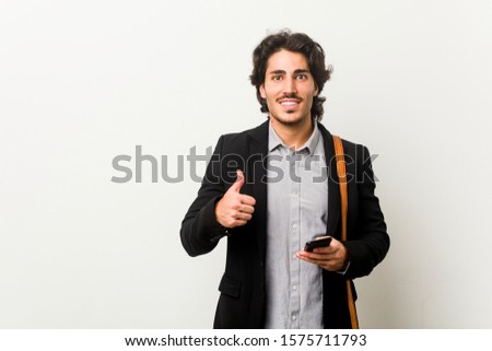 Young business man holding a phone smiling and raising thumb up