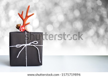 Hand craft Christmas gift box wrap by black paper decoreted with antler on silver bokeh background.