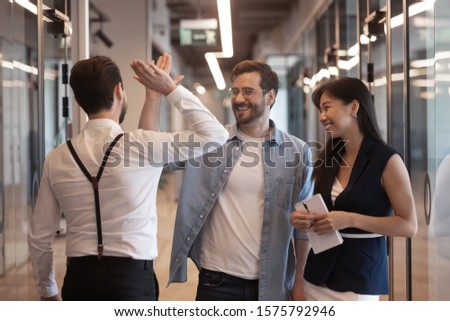 Three workers standing in office hallway talking, millennial guys caucasian businessmen colleagues meet greeting glad to see each other giving high five gesture of respect friendly relations concept Royalty-Free Stock Photo #1575792946