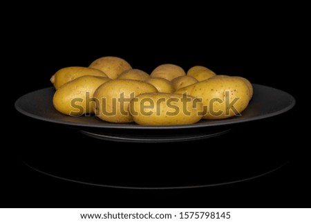 Lot of whole pale yellow potato on gray ceramic plate isolated on black glass