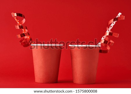 Two paper coffee cups with decorations and straw on red backgrond. Valentines day festive concept