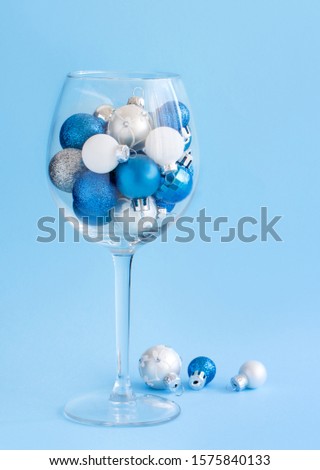 Christmas baubles in a wine glass on a light blue background close up