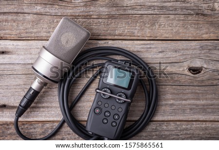Large diaphragm condenser studio microphone and recorder on a wooden background.