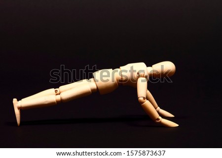 Conceptual image of a wooden manikin doing push ups isolated on a black background