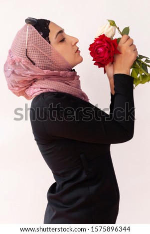 Stylish Muslim woman in traditional Islamic clothing holding flower bouquet. Portrait of beautiful middle-eastern girl in Hijab. Stock photo of Islamic clothing, fashion. Isolated on white background