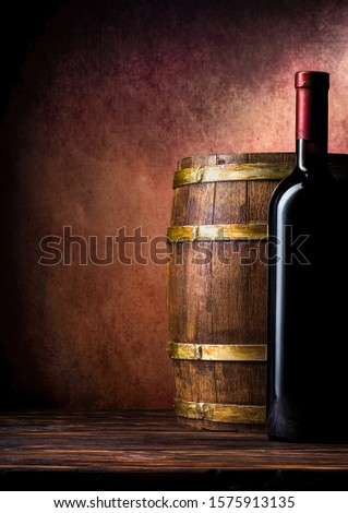 Bottle of red wine and barrel on burgundy background