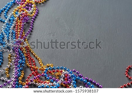 Long glossy different color beads scattered on dark concrete table. Space for text