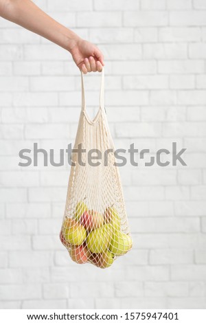 Female hand holding organic pears in zero waste net bag over white bricks wall background