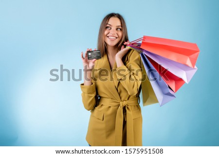 cheerful woman holding credit card and colorful shopping bags looking at copyspace isolated over blue