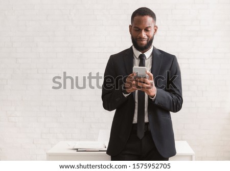 Happy black man in suit chatting on smartphone while having break at job, white background, copy space