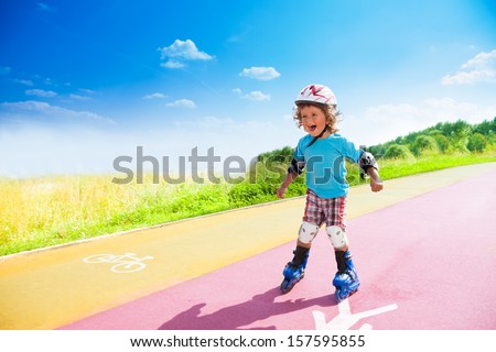 Happy thee years old boy rollerblading in the park on sunny summer day with bike and pedestrian signs on the road