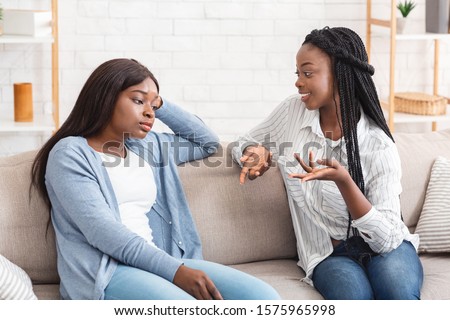 Talkative friend concept. Young black woman tired of her girlfriend talking non-stop while they sitting together on sofa at home Royalty-Free Stock Photo #1575965998