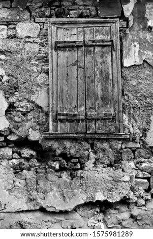 Textured wall of old run-down house with window closed by shutters. Black and white architectural detail