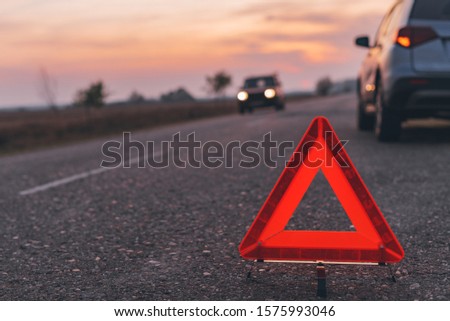 Warning triangle sign on the road in sunset by the broken car, selective focus
