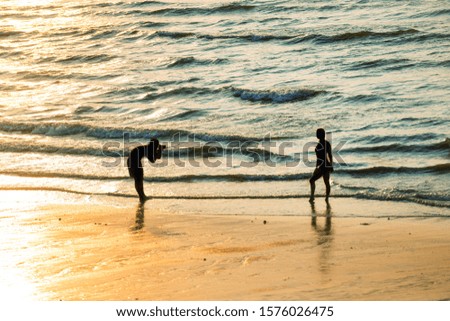 Silhouettes of people walking on beach and taking photo at beautiful sunset
